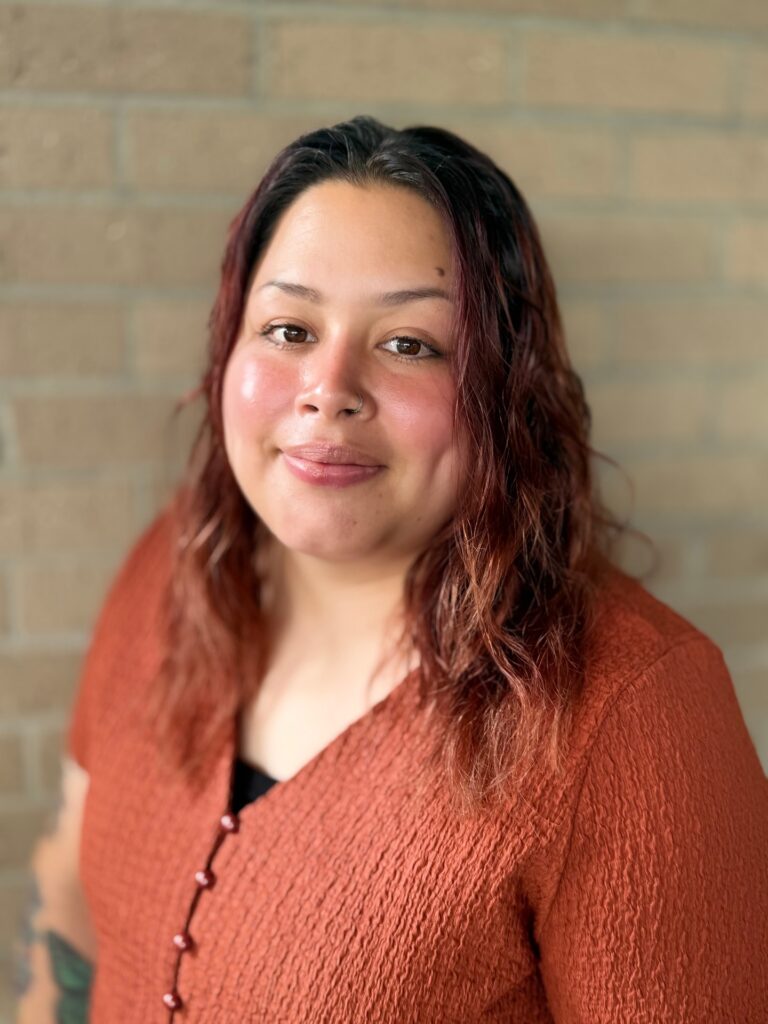 Portrait of Ms. Ivy wearing a rust-colored top against a brick wall.