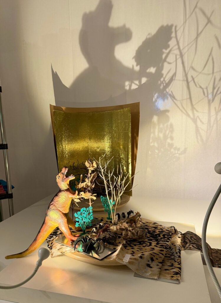 Toy dinosaur and forest figures cast large shadows on a wall in a classroom light-table display.